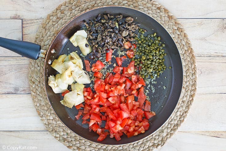 artichoke hearts, olives, tomatoes, and capers in a skillet