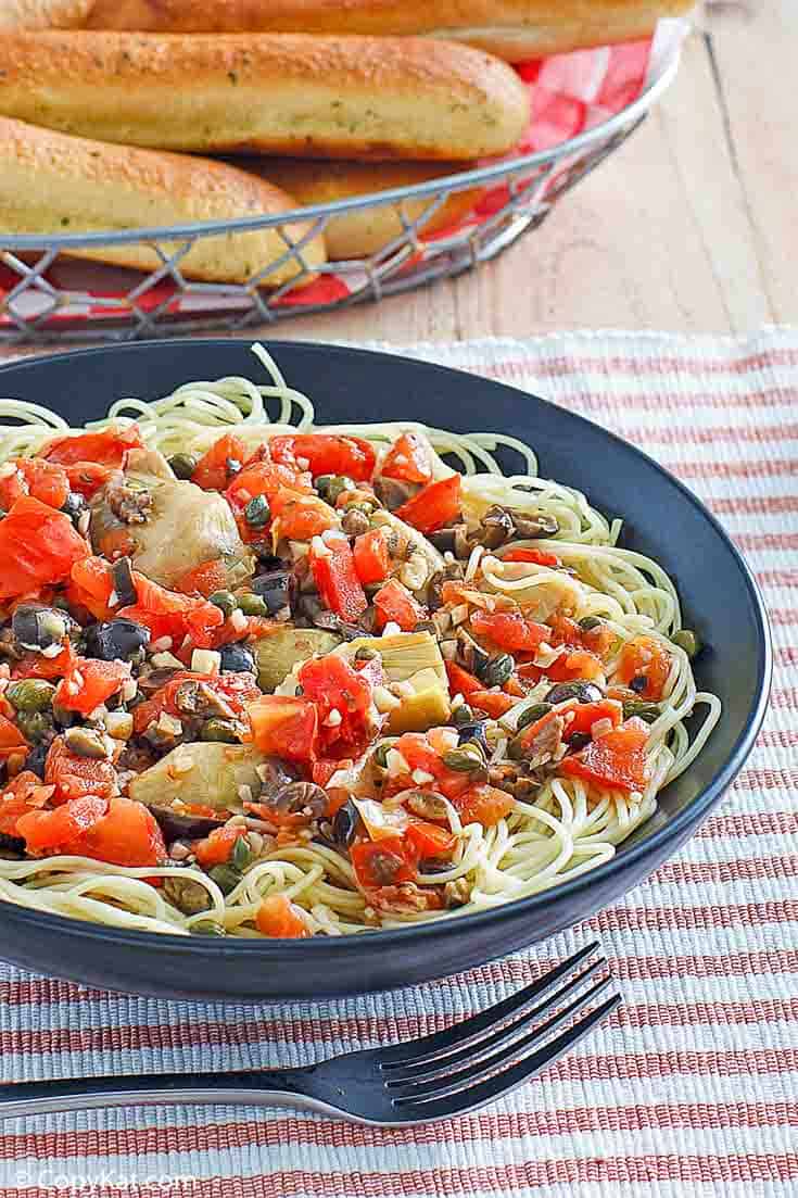 a bowl of angel hair pasta with artichokes, olives, tomatoes, and garlic