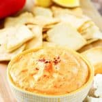 a bowl of roasted red pepper dip next to crackers
