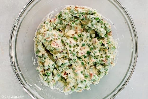 peas, carrots, bacon, and ranch dressing together in a glass bowl