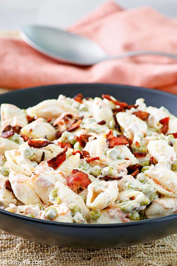 a bowl of pasta salad with bacon, carrots, peas, and ranch dressing