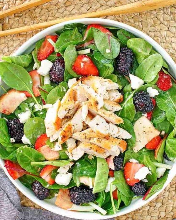 a bowl of salad with chicken, berries, and feta cheese