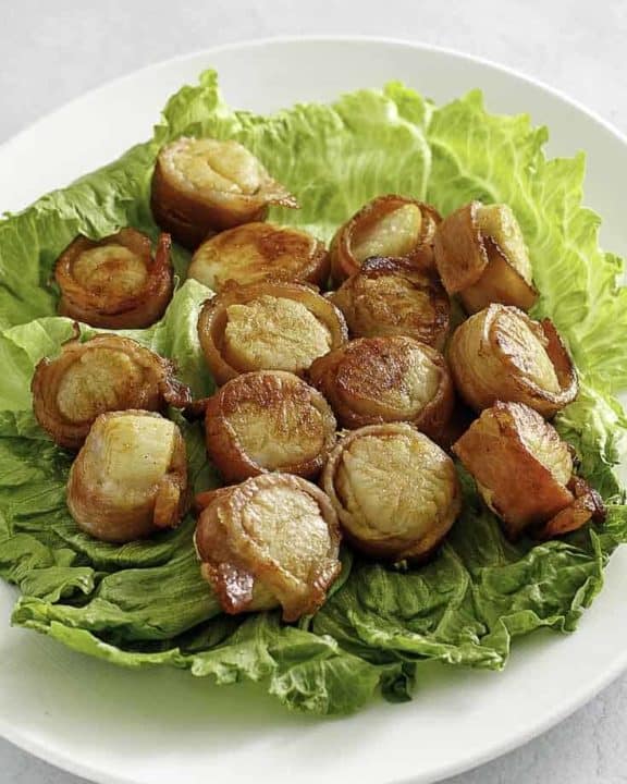 bacon wrapped scallops on top of lettuce on a platter