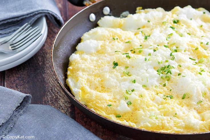 a fluffy omelette in a pan next to forks, plates, and blue napkins