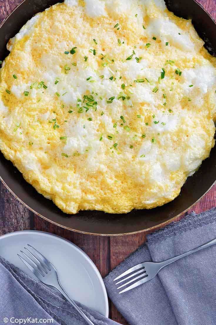 fluffy omelette in a skillet next to forks and napkins