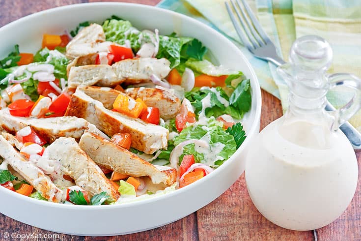 Homemade Old Spaghetti Factory creamy pesto dressing in a bottle next to a bowl of salad