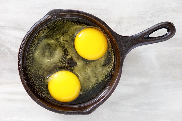 two raw cracked eggs in a cast iron skillet