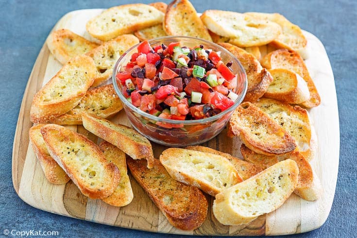 homemade crostini on a platter with a bowl of tomato topping