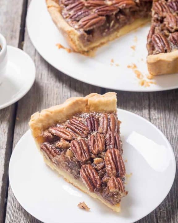a slice of pecan pie on a white plate next to the pie