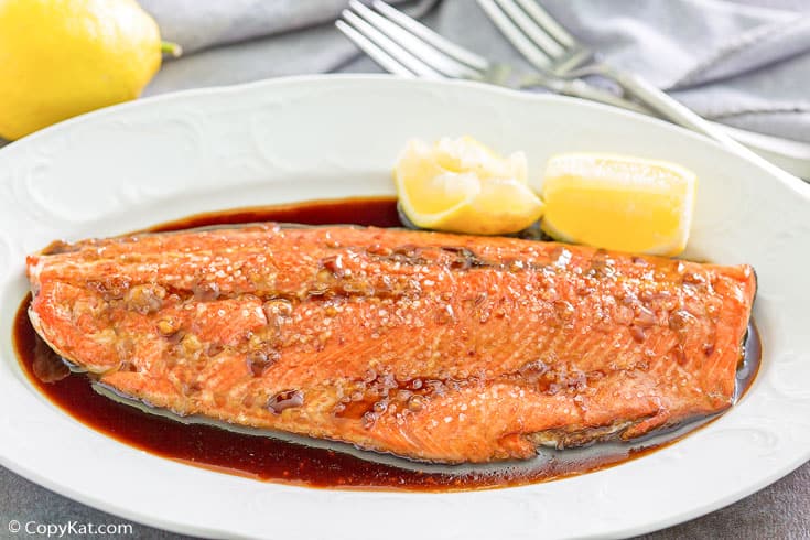 baked salmon with sauce and lemon wedges on a white platter