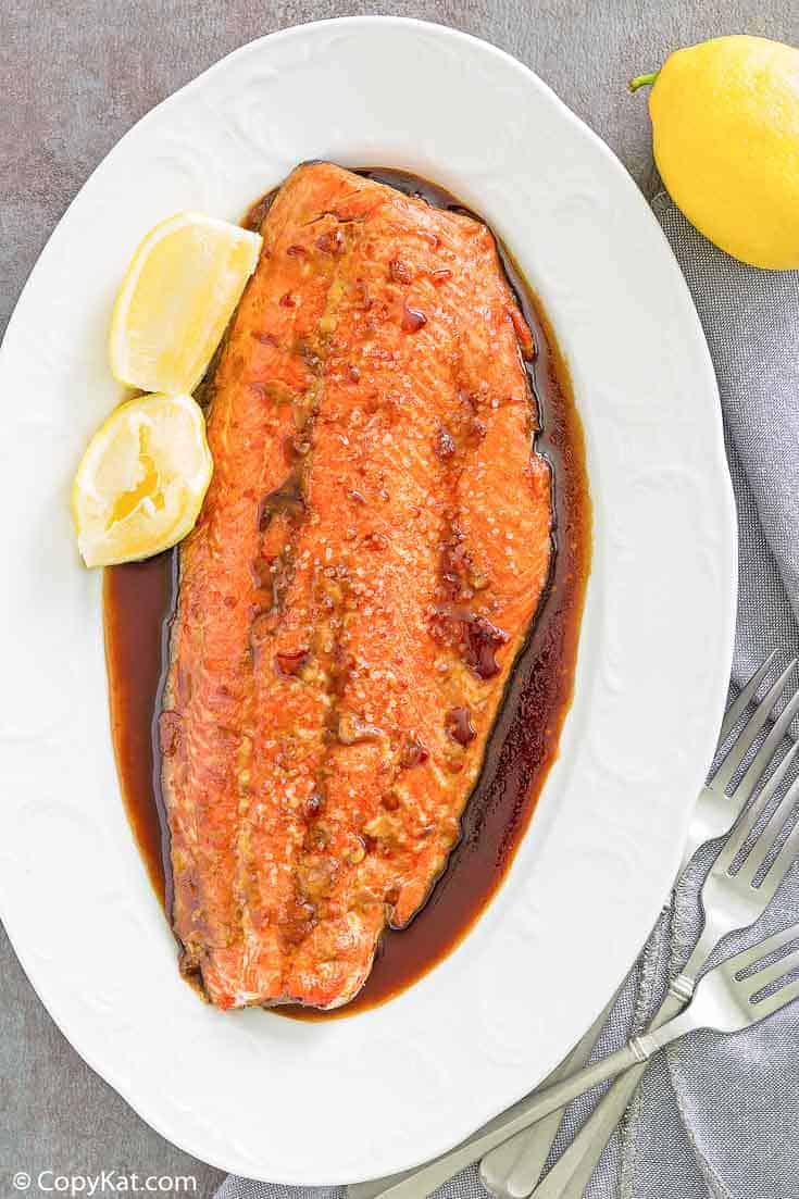 baked salmon with sauce and lemon wedges on a platter