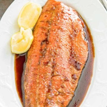 baked salmon, sauce, and lemon wedges on a platter