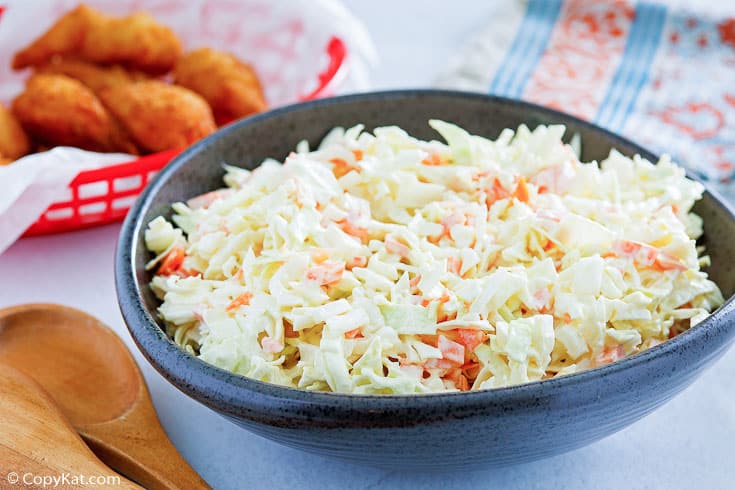 A bowl of cole slaw next to a basket of hush puppies