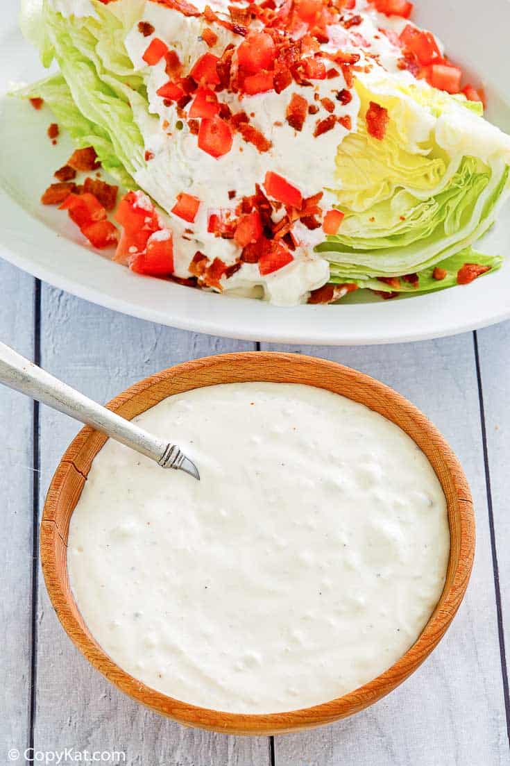 a bowl of blue cheese dressing next to a wedge salad