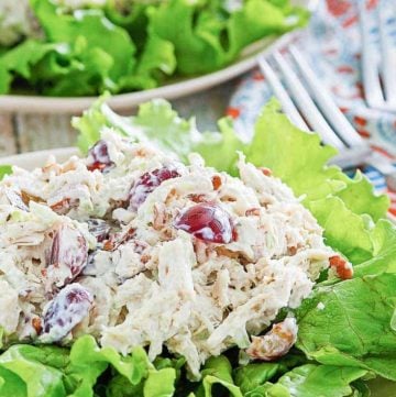 chicken salad with grapes, apples, and pecans on top of lettuce on a plate