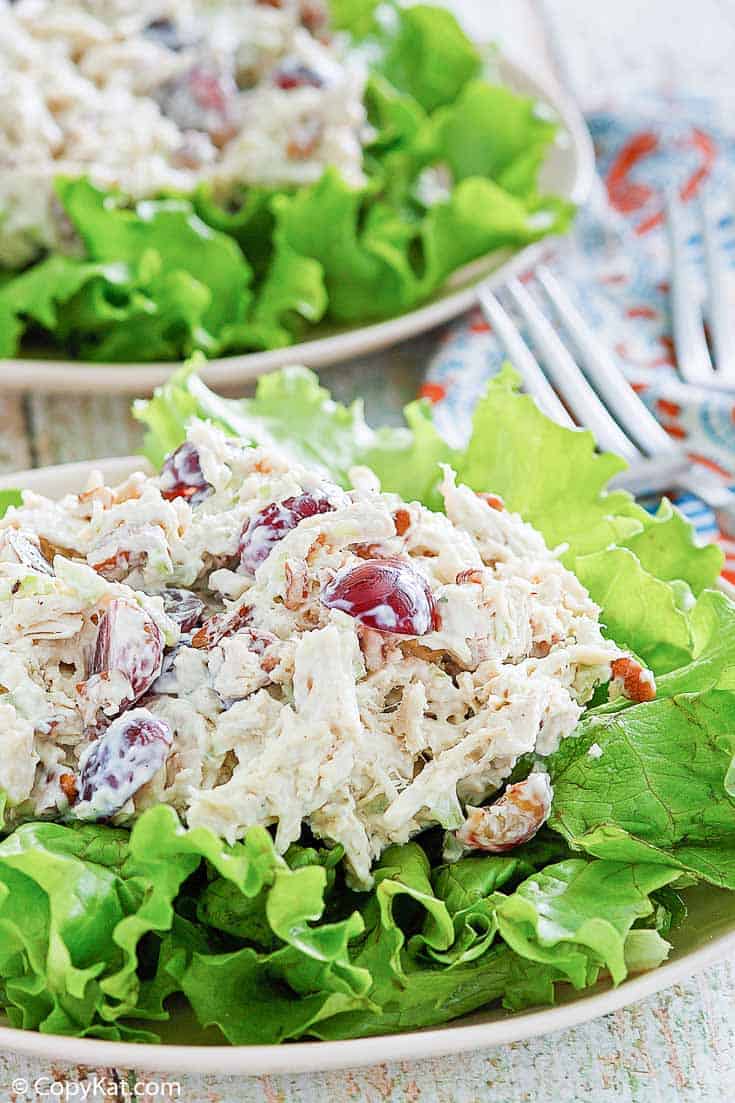 chicken salad with grapes, apples, and pecans on top of lettuce on a plate