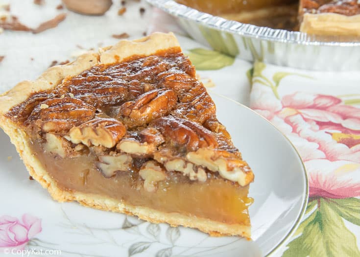 a slice of homemade pecan pie on a white plate with pink flowers