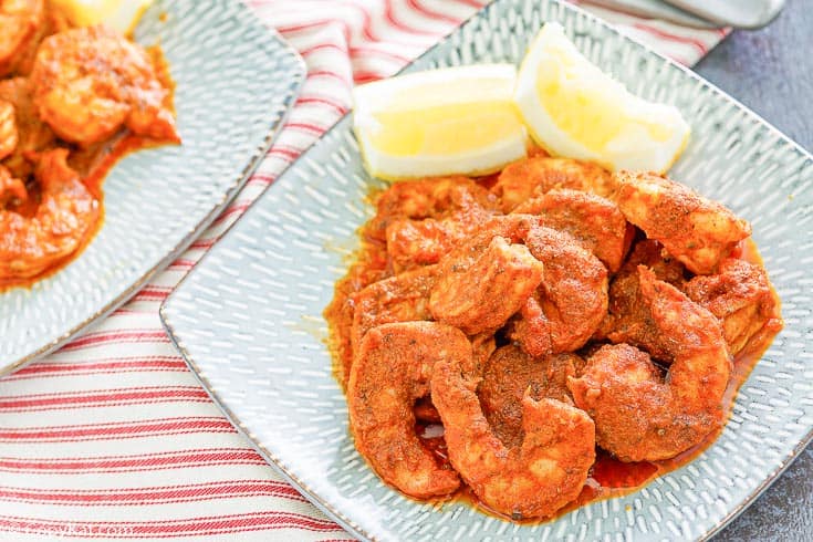 Cajun shrimp and lemon wedges on a blue plate