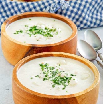 Two bowls of homemade Red Lobster clam chowder, two spoons, and a basket of bread slices