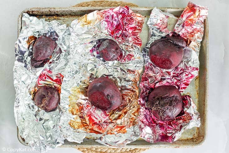roasted whole beets in foil on a baking sheet