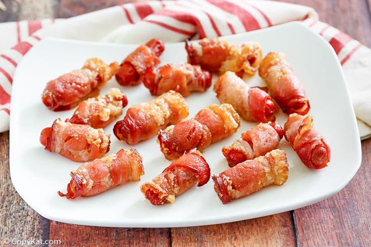 brown sugar bacon wrapped little smokies on a platter next to a kitchen towel