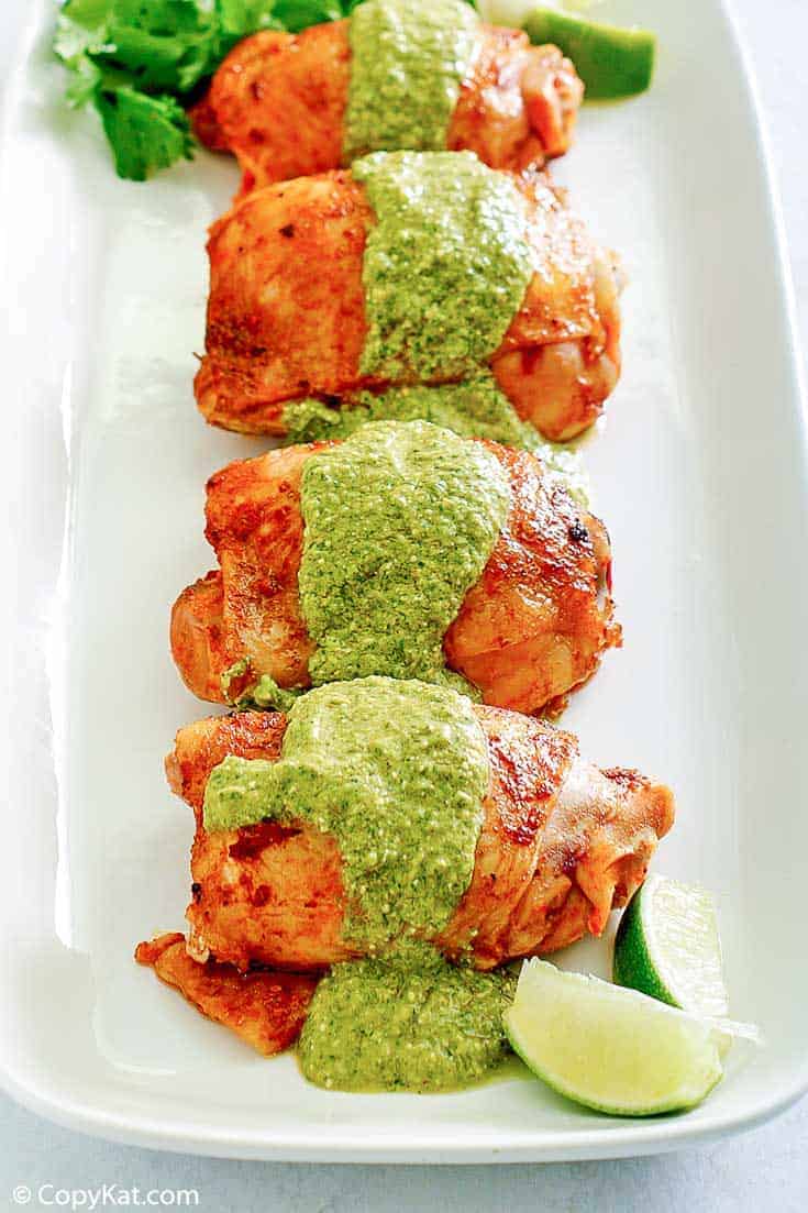 four Peruvian chicken thighs with green sauce on a platter