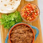 overhead view of beef barbacoa, cilantro, salsa, tortillas, and sour cream