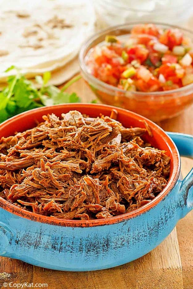 a bowl of homemade Chipotle Mexican Grill Barbacoa beef, salsa, tortillas, and sour cream