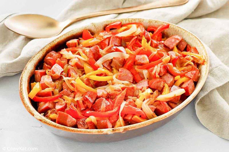 a spoon next to a dish of sausage and peppers