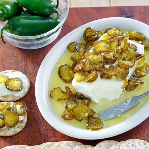 candied jalapenos over cream cheese on a platter next to crackers