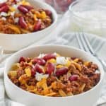 two bowls of Cincinnati chili topped with cheese, onions, and kidney beans