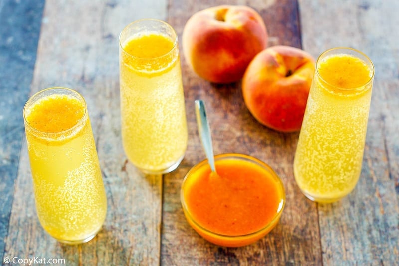 three homemade Harry's Bar Bellini drinks, two fresh peaches, and a bowl of peach puree