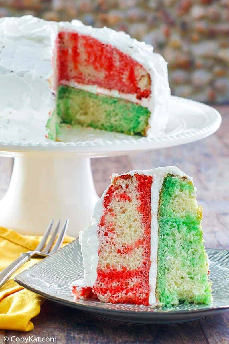 a slice of Jello poke cake in front the the cake on a stand