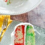 a slice of red and green Jello poke cake with Cool Whip frosting