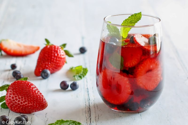 a glass of berry sangria, strawberries, blueberries, and mint leaves