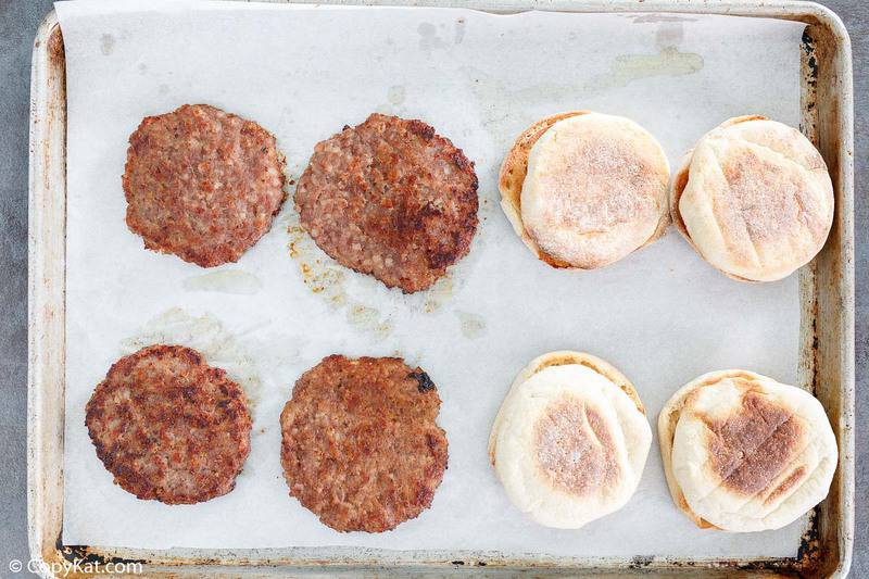 cooked sausage patties and toasted English muffins on a baking sheet