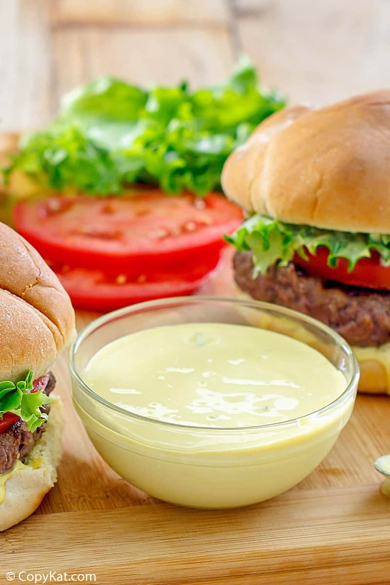 a bowl of homemade smash sauce, a burger, tomato slices, and lettuce