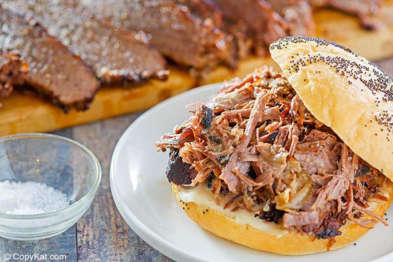 a brisket sandwich on a plate and brisket slices on a cutting board