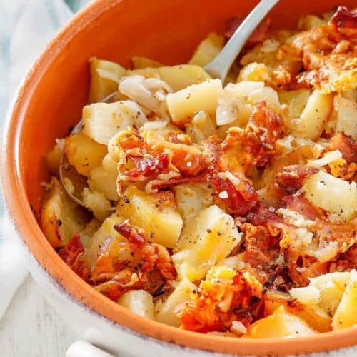 Crockpot cheesy potatoes with bacon and a spoon in a bowl