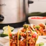 three chicken tacos in front of a crockpot