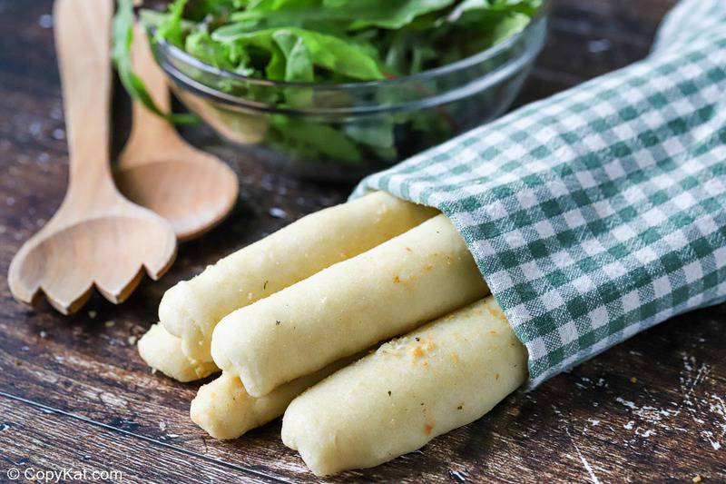 homemade Olive Garden breadsticks wrapped in a kitchen towel, salad tongs, and a salad