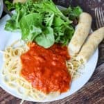 Homemade Olive Garden breadsticks, spaghetti with marinara, and salad greens on a plate