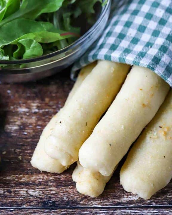 Homemade Olive Garden breadsticks wrapped in a kitchen towel and a salad