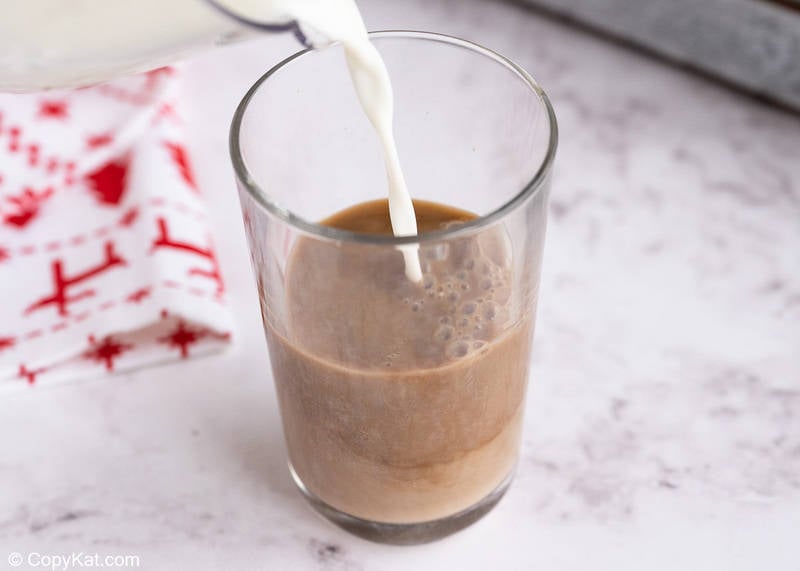pouring steamed milk into a glass with peppermint mocha and coffee