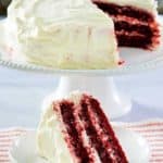 homemade Waldorf Astoria Red Velvet Cake slice on a plate in front of the cake on a stand