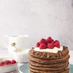 a stack of chocolate pancakes, raspberries, and cream