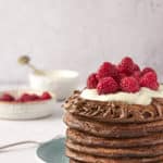 a stack of six chocolate pancakes topped with whipped cream and raspberries
