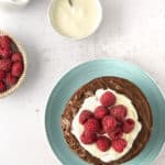 overhead view of chocolate pancakes topped with chocolate spread, whipped cream, and raspberries
