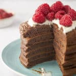 stack of chocolate pancakes topped with whipped cream and raspberries with a wedge cut out