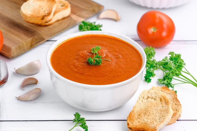Instant Pot tomato soup in a bowl, toasted bread, parsley, garlic, and a tomato